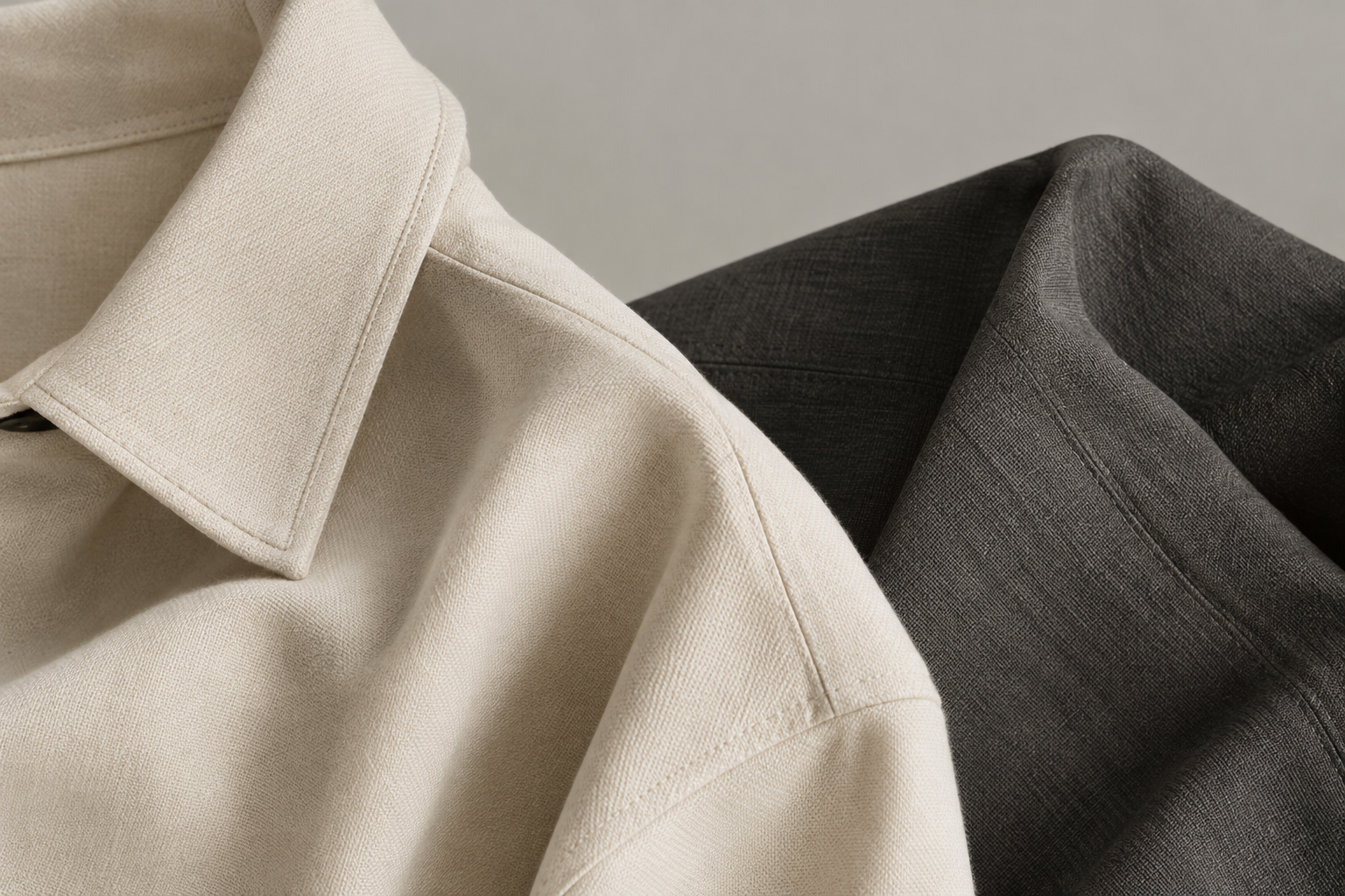 Editorial close-up of a cream and charcoal garment detail showing refined stitching and soft woven texture