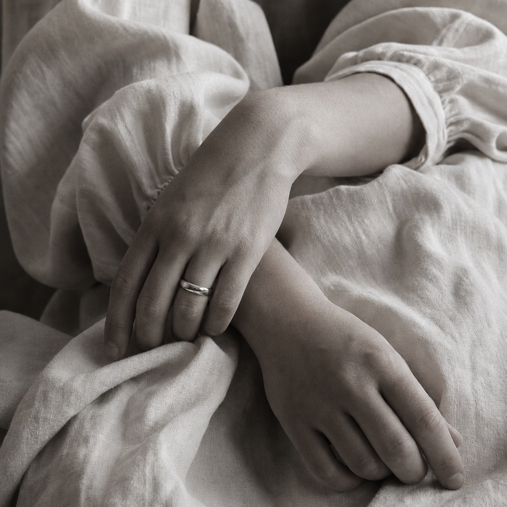 Close-up detail of hands resting on textured linen fabric with subtle skin highlights and grainy monochrome styling
