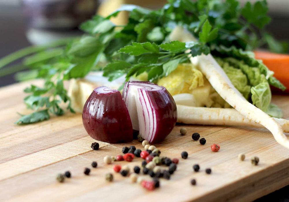 Red onion, peppercorns and fresh herbs on a wooden chopping board