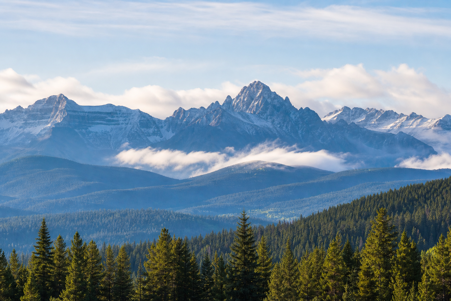 Wide view of blue-toned Colorado mountains with soft clouds and evergreen foothills