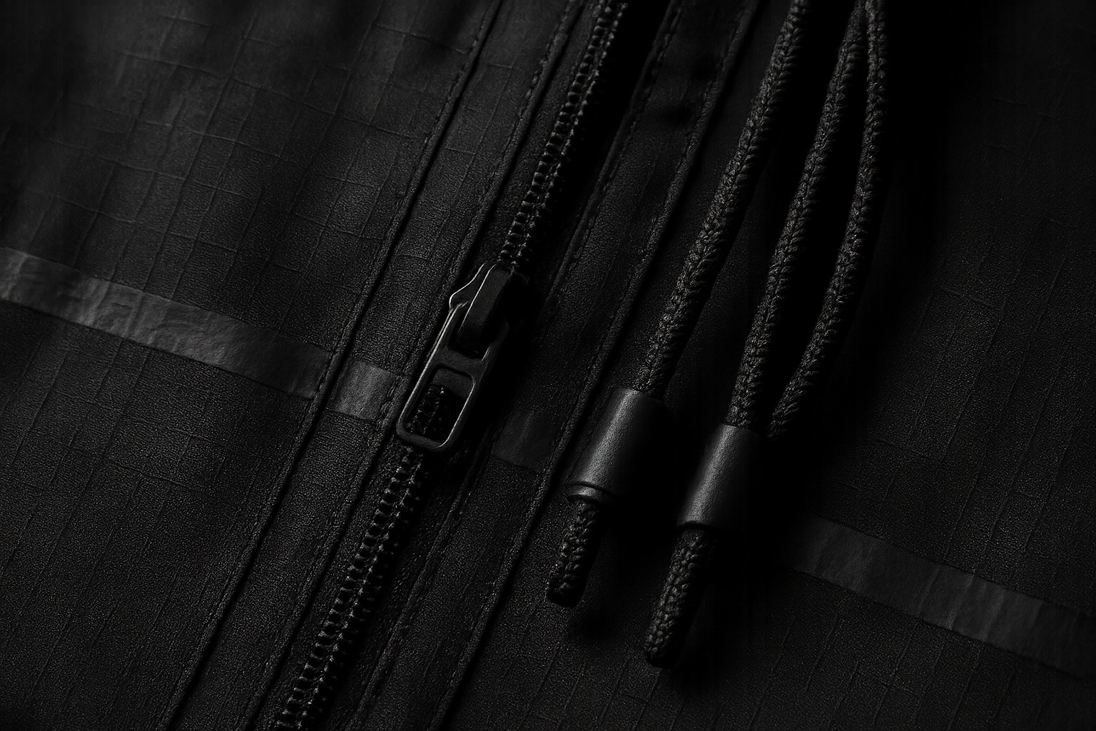 Macro shot of black ripstop, taped seams, and metal pullers lit with directional studio light