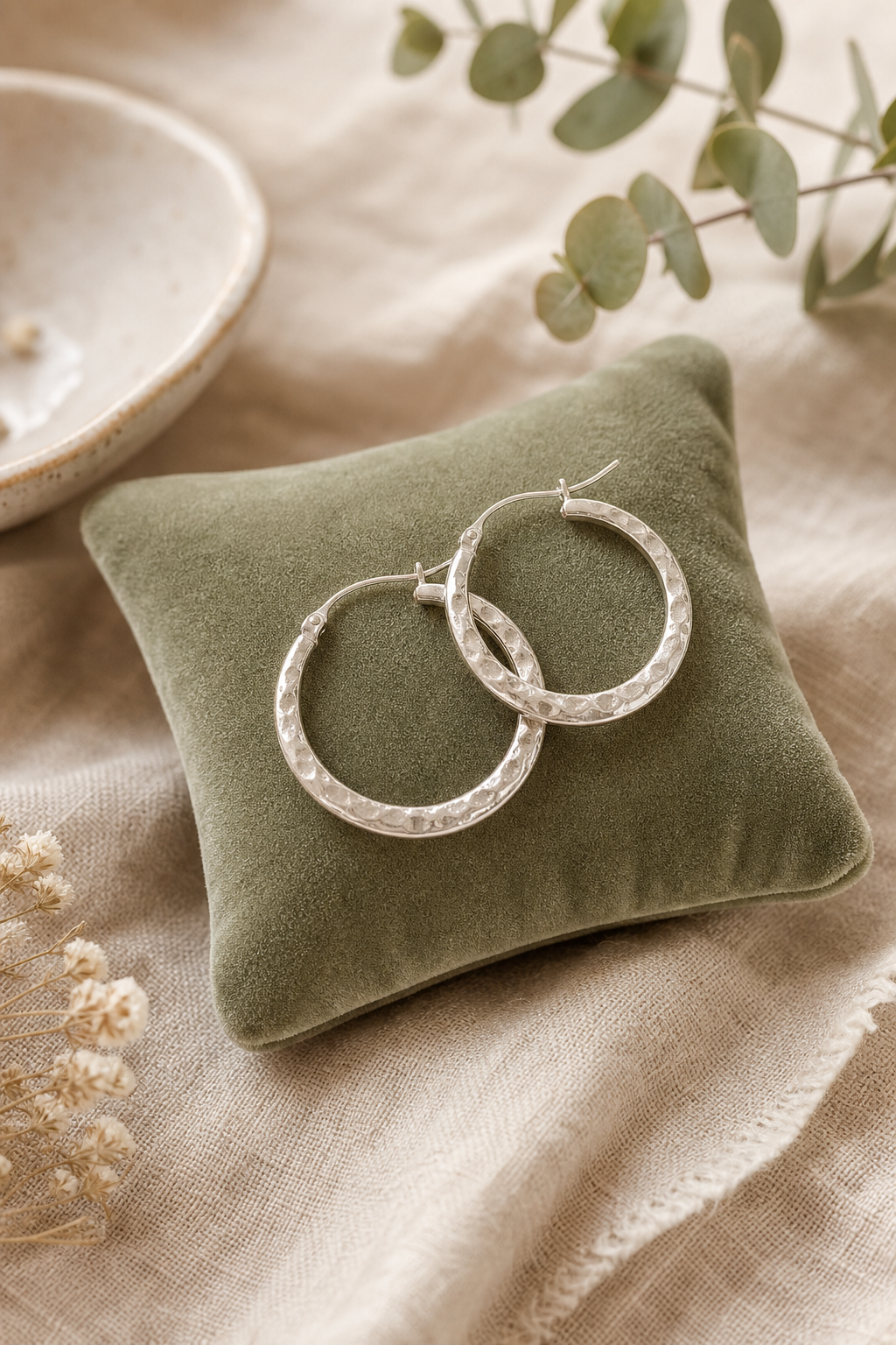 Pair of handmade hammered silver hoop earrings resting on a sage-green velvet pillow