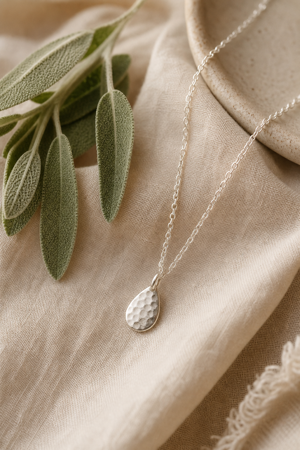 Delicate handmade silver necklace with a hammered teardrop pendant on linen