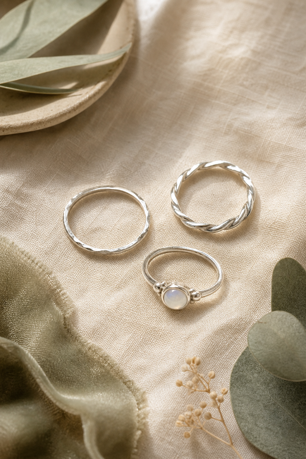 Flat-lay of three handmade silver rings styled on warm linen