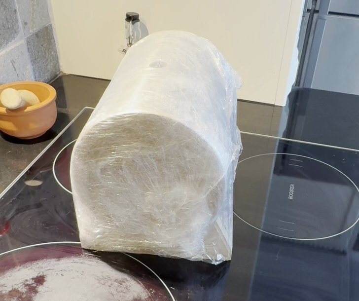 Wrapped cylindrical Crafthouz component resting on a dark workshop stovetop, showing early-stage protection and handling