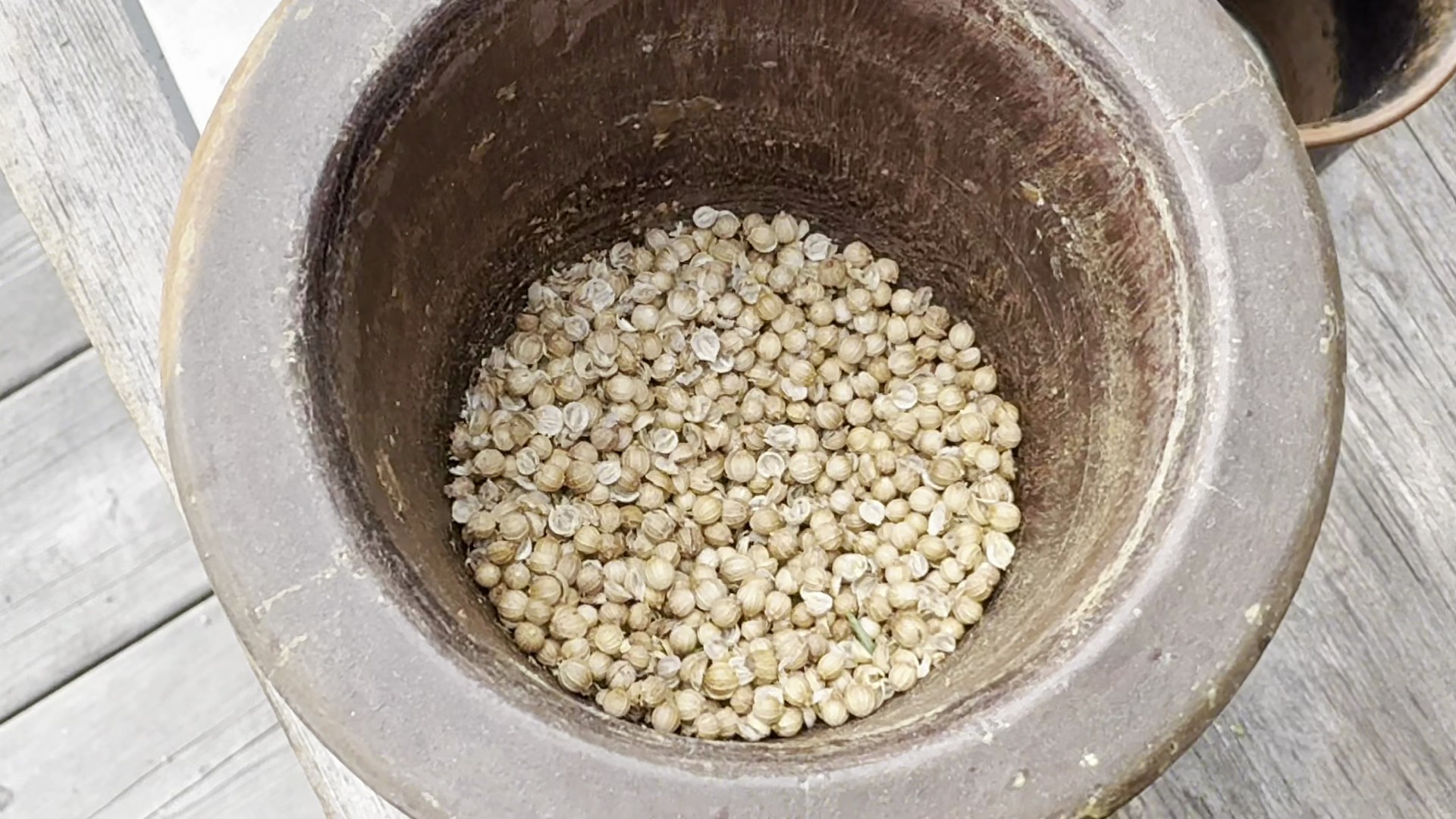 Top-down view into a rustic vessel filled with coriander seeds on a wooden surface