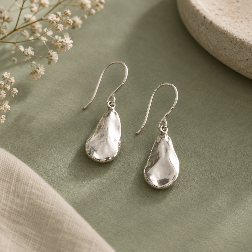 Handcrafted silver earrings on a soft sage-toned surface