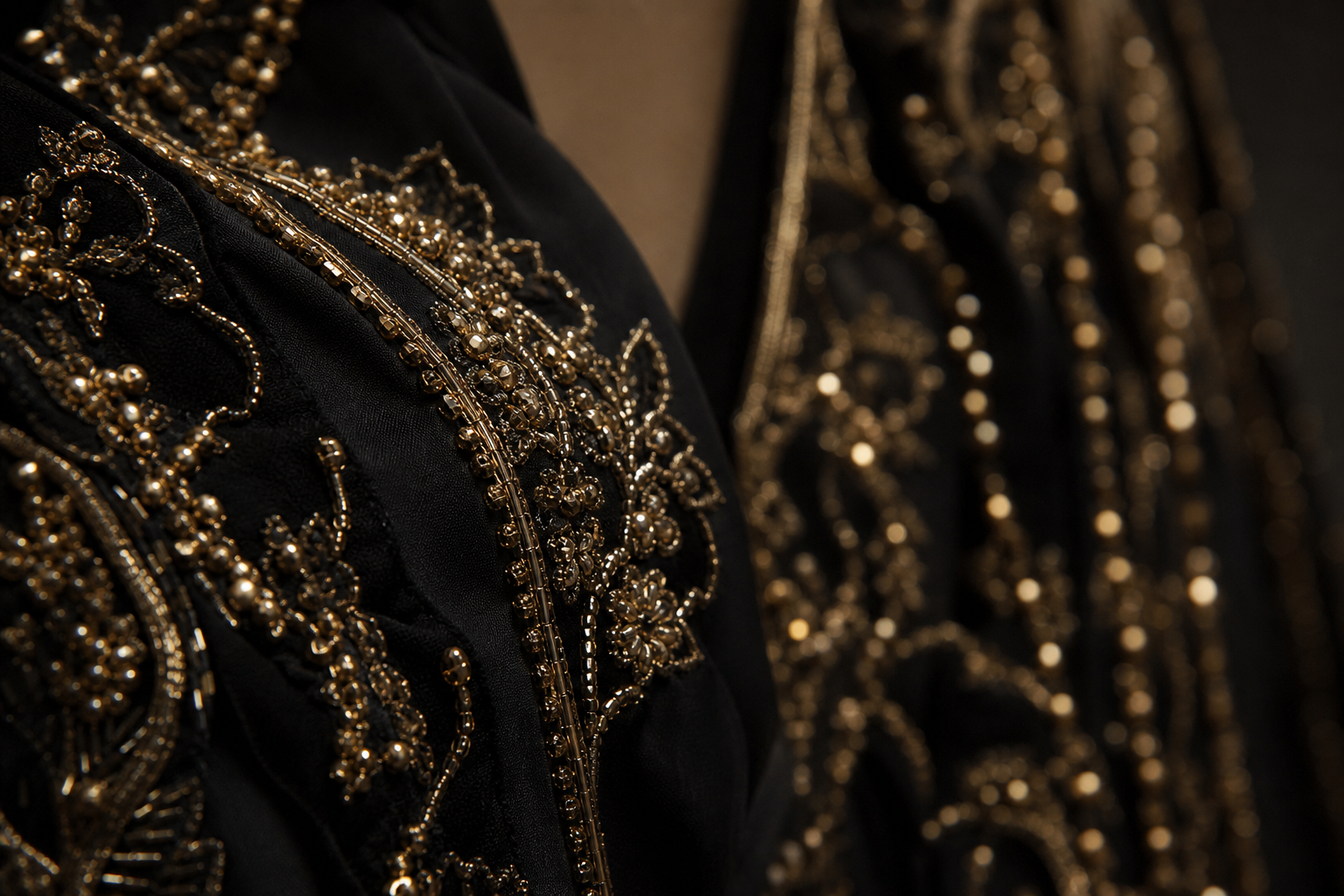 Editorial close-up of black couture fabric with gold beading and soft cinematic lighting