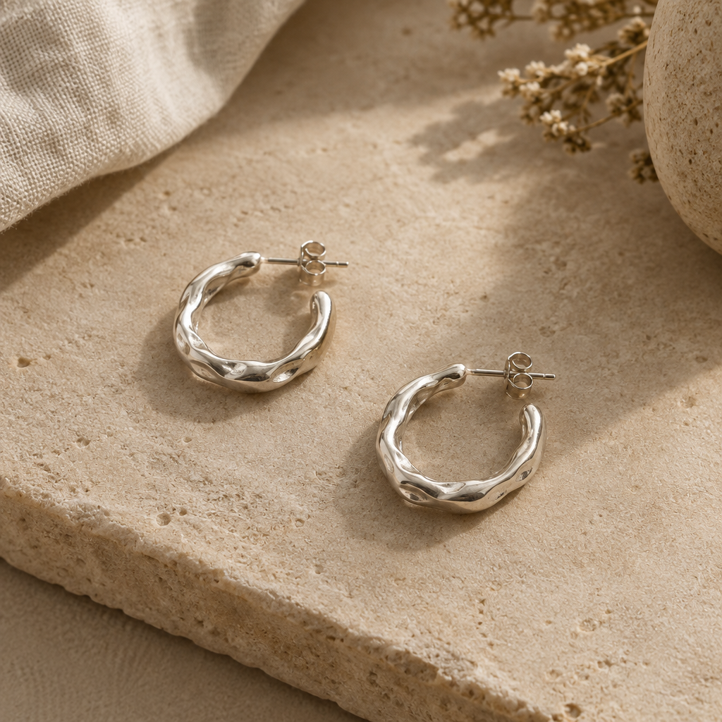 Small organic sterling silver hoop earrings against a warm neutral surface