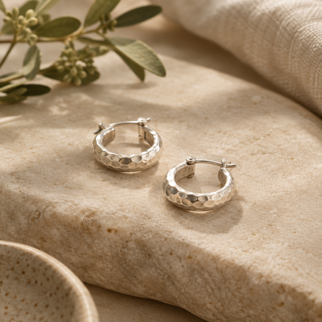 Small hammered silver hoop earrings on a warm stone surface