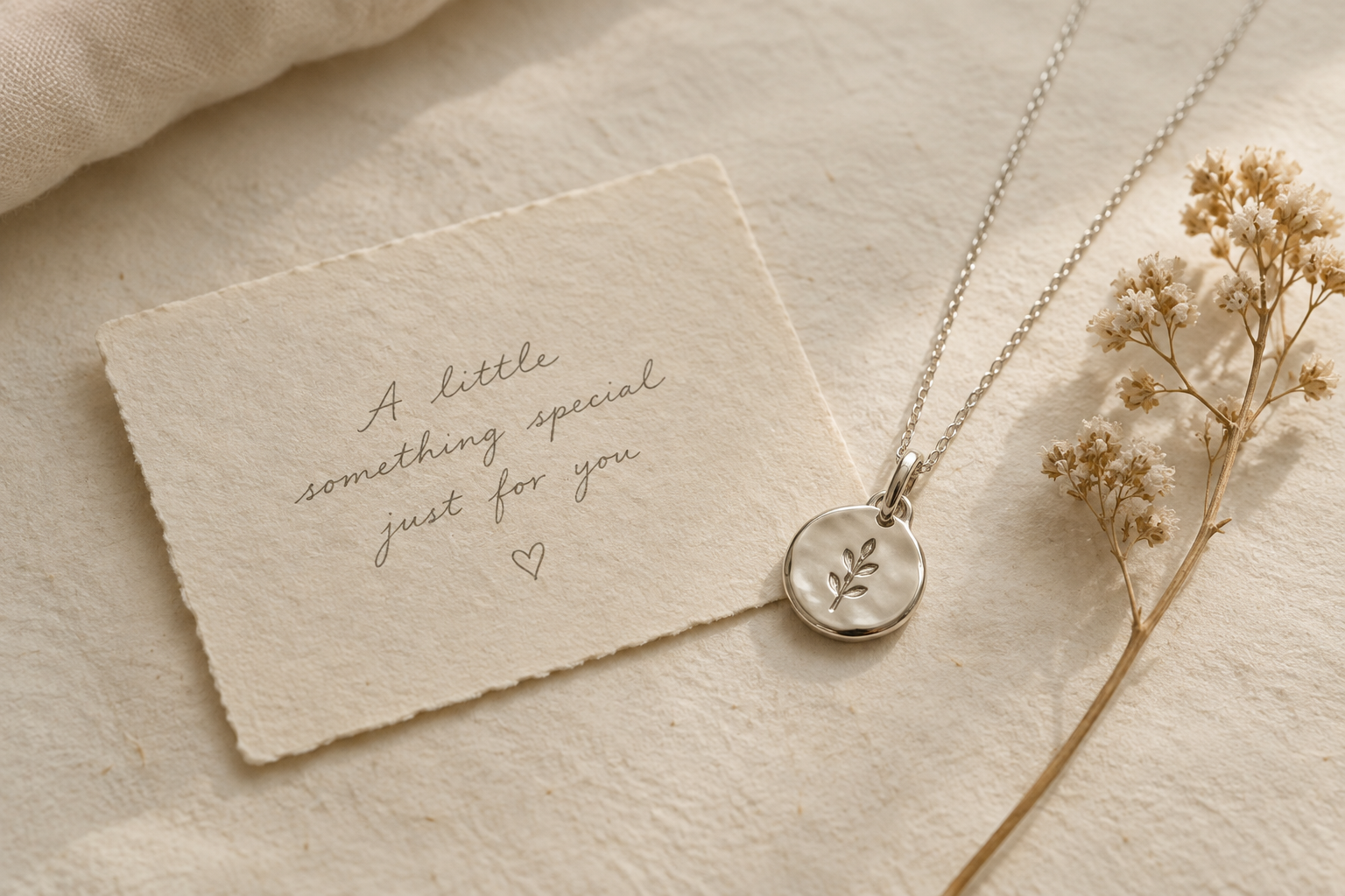 Cream handwritten gift note beside a small polished silver pendant and dried botanical stem