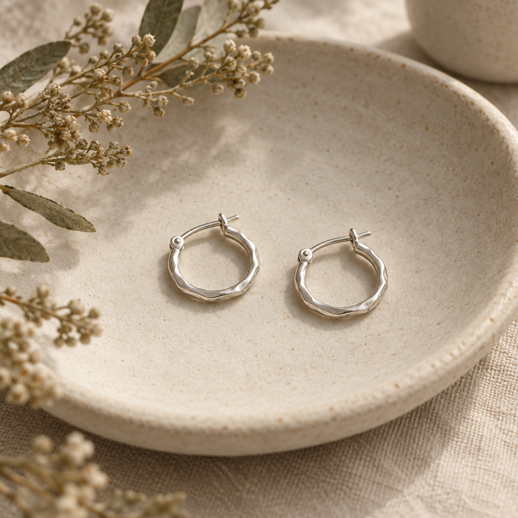 Pair of small organic sterling silver hoop earrings on a pale ceramic dish
