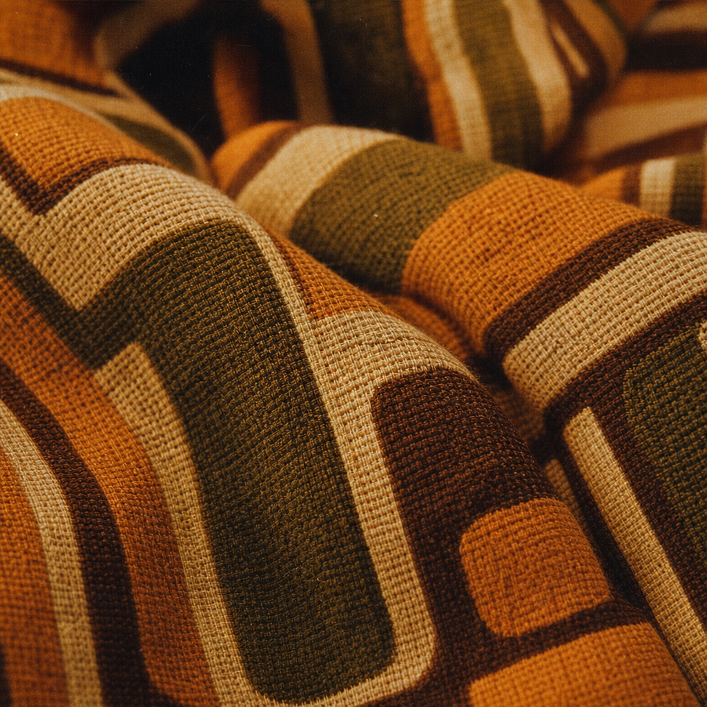 Close-up of textured vintage fabric in a warm amber palette with visible weave and retro pattern