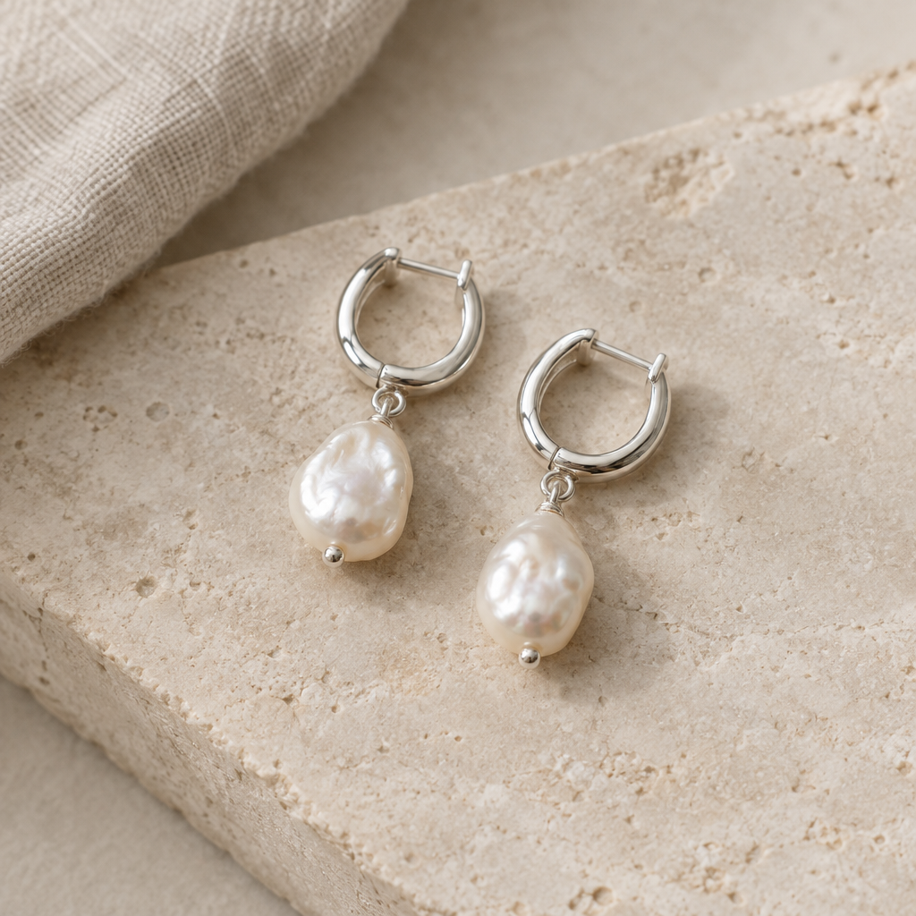 A pair of silver hoops with freshwater pearl drops on a pale stone surface