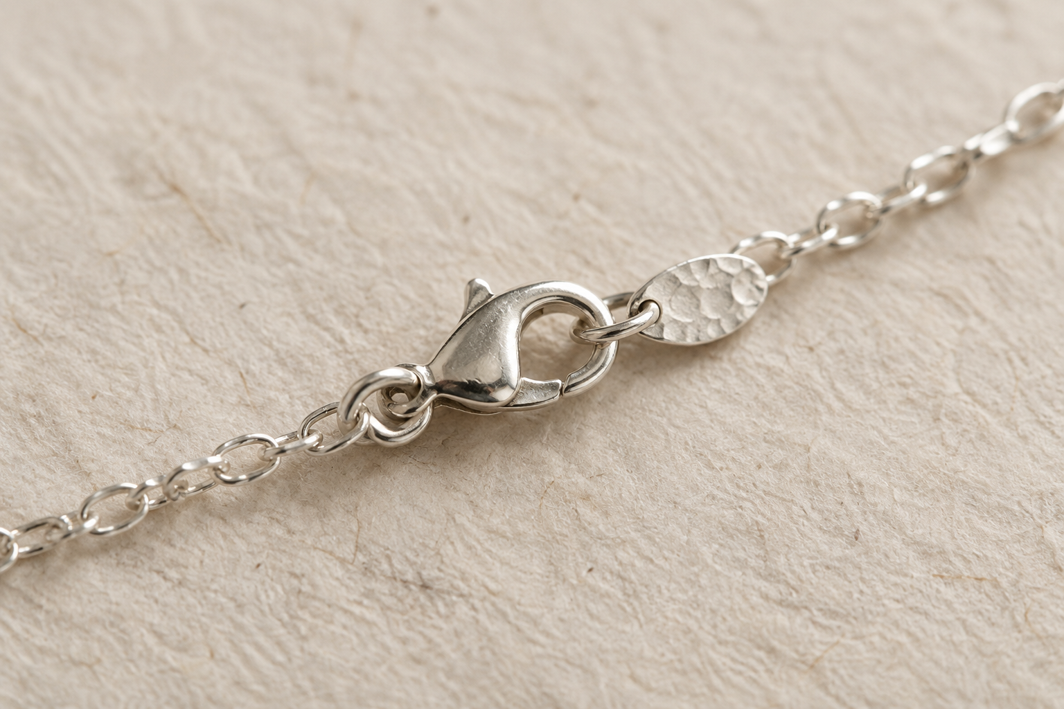 Close-up of a handmade silver necklace clasp and finely textured links on artisan paper