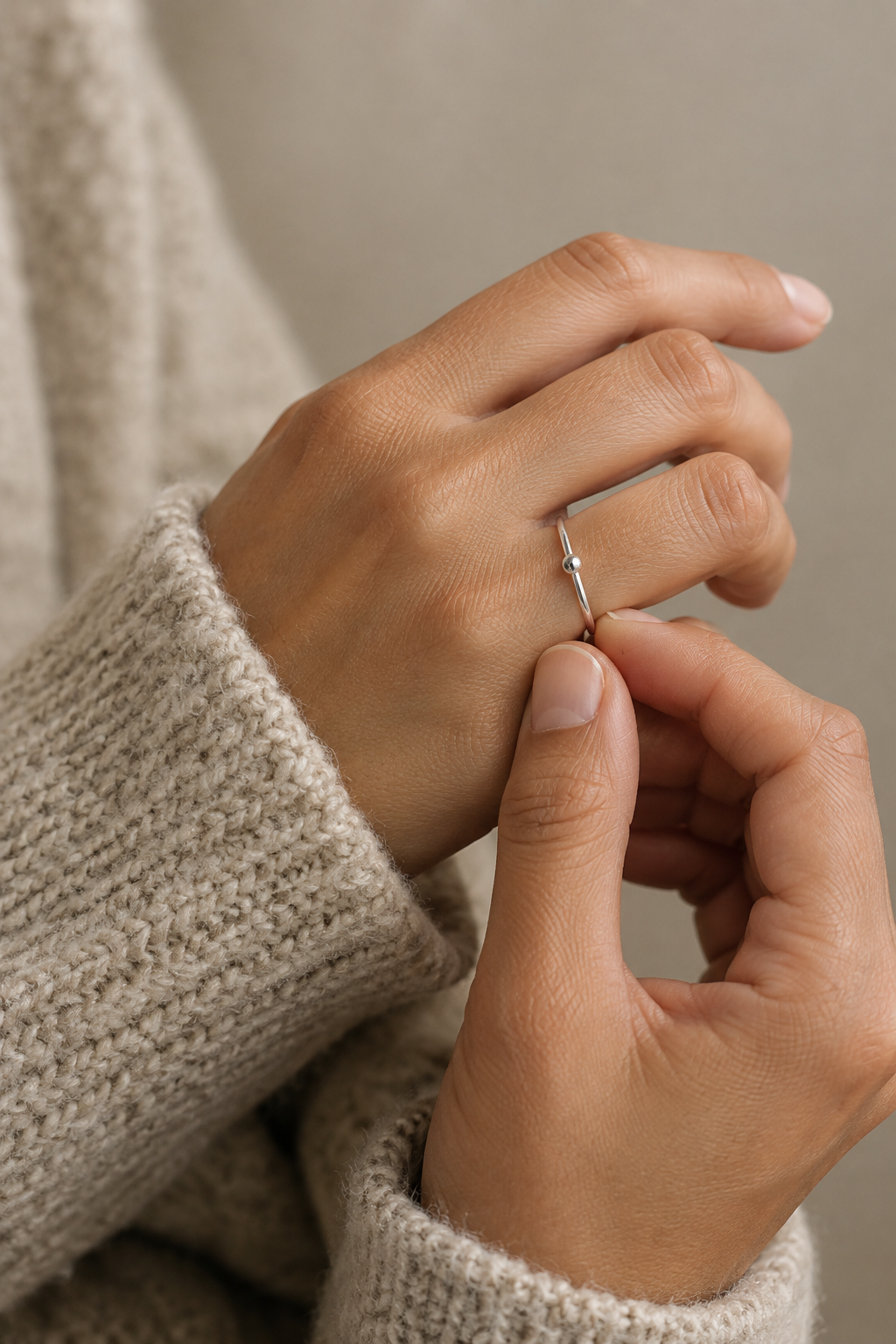 Hands gently styling a delicate silver ring beside a soft knitted sleeve