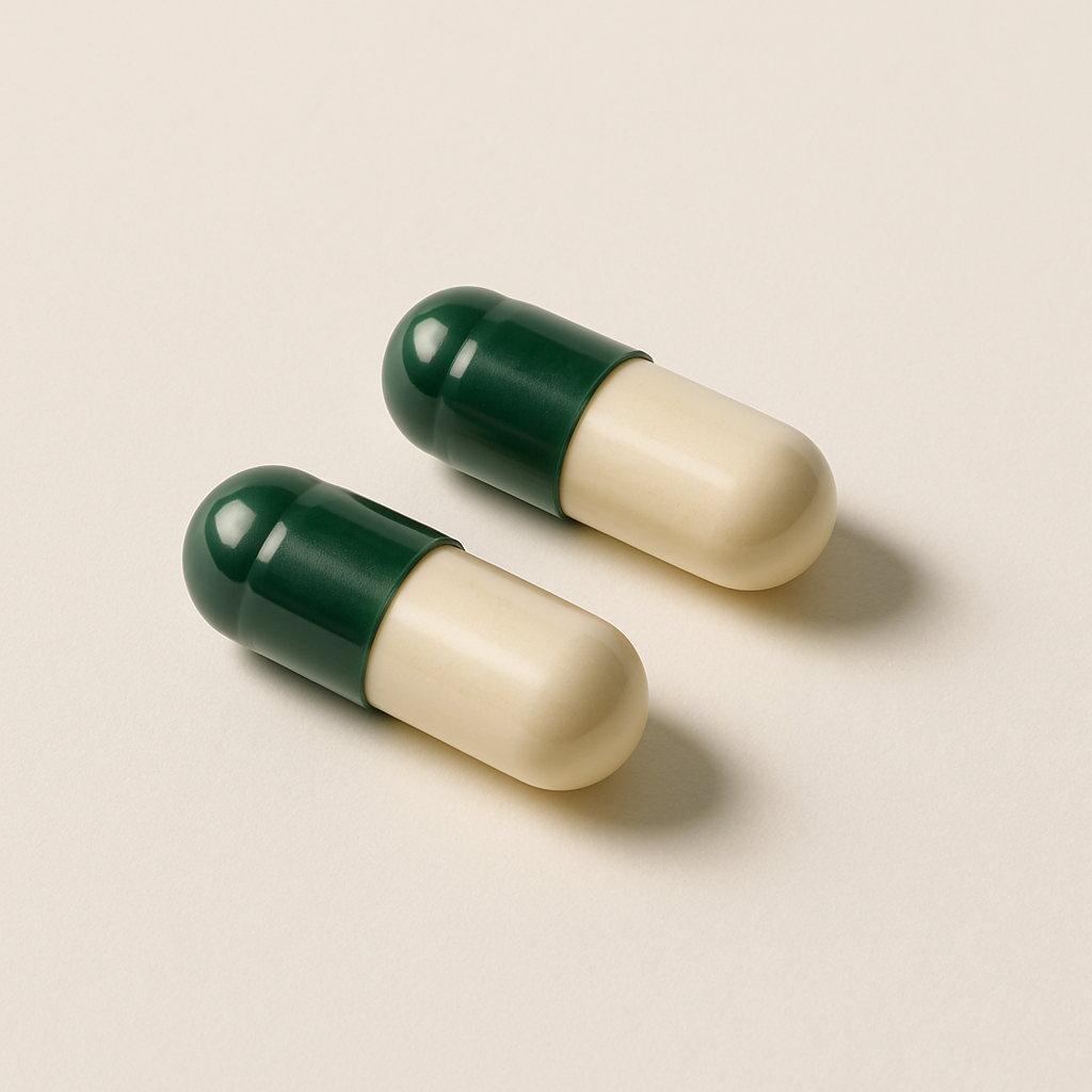 Two-tone plant-based capsules in deep forest green and warm off-white on a minimal studio surface with soft shadows.