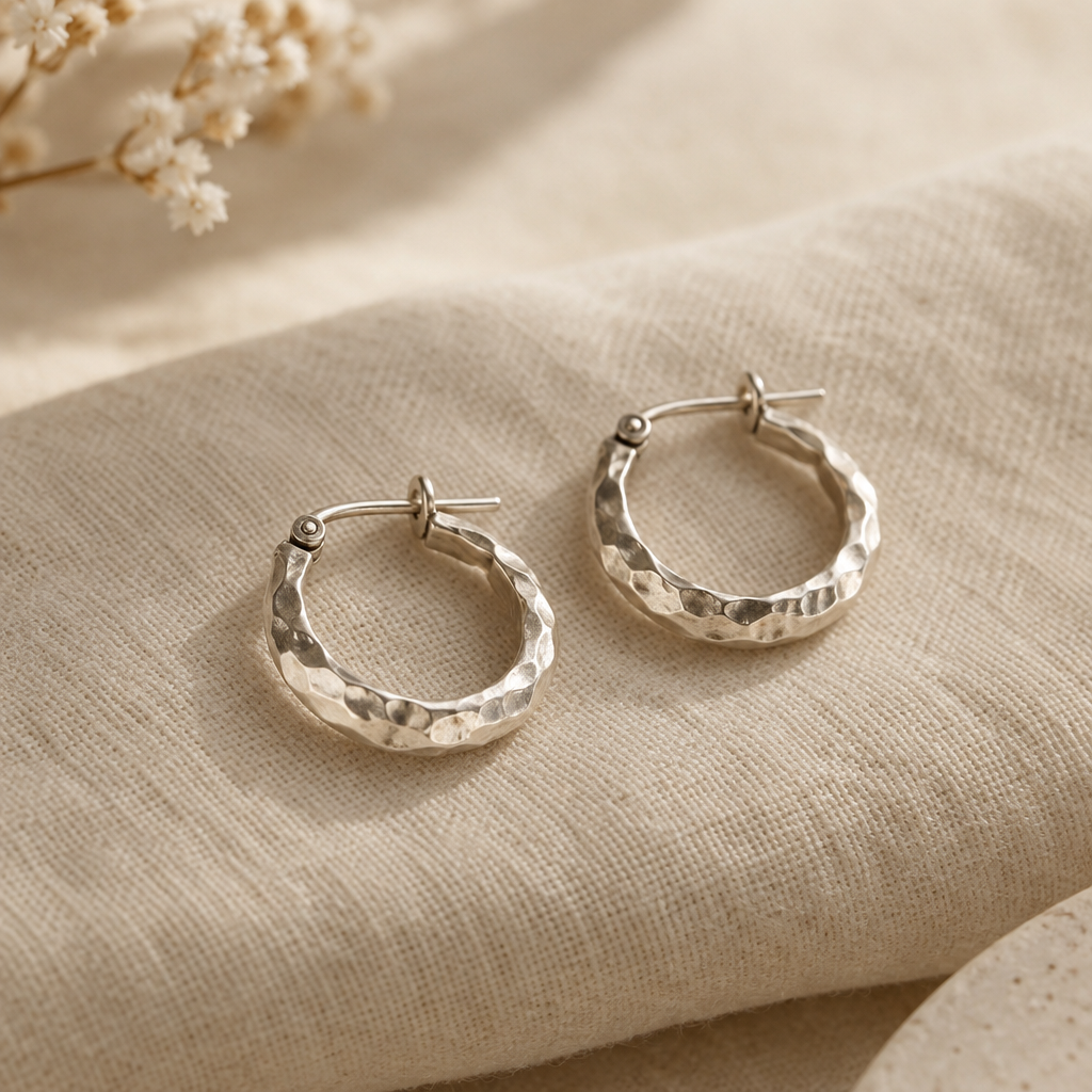 A pair of small hammered silver hoop earrings with a softly irregular finish