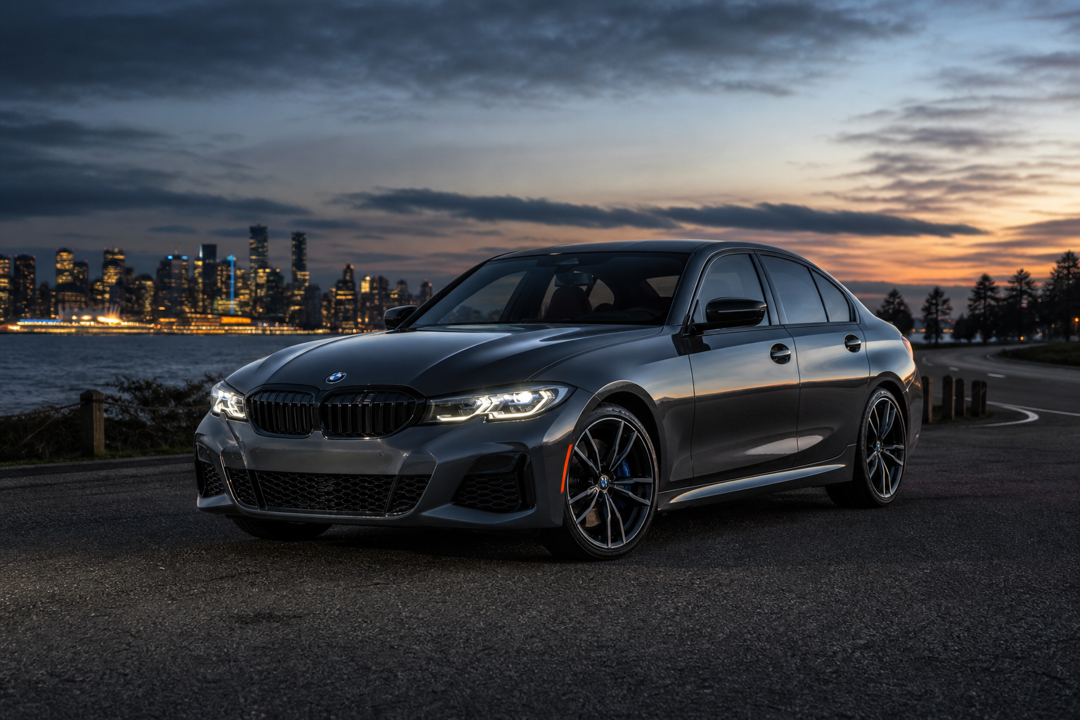 Metallic graphite BMW M340i xDrive parked at dusk on a coastal highway with city lights behind