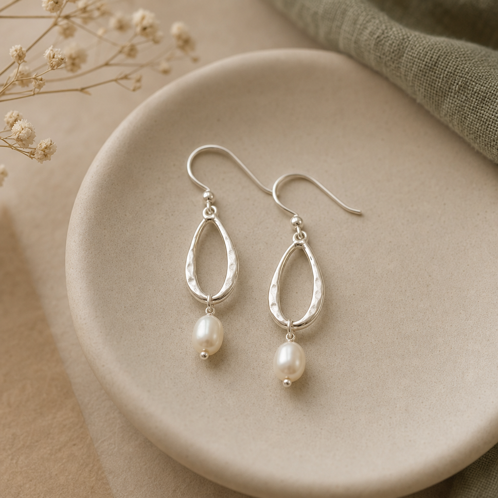 Pair of dangling silver drop earrings with small pearls laid on a rounded ceramic dish