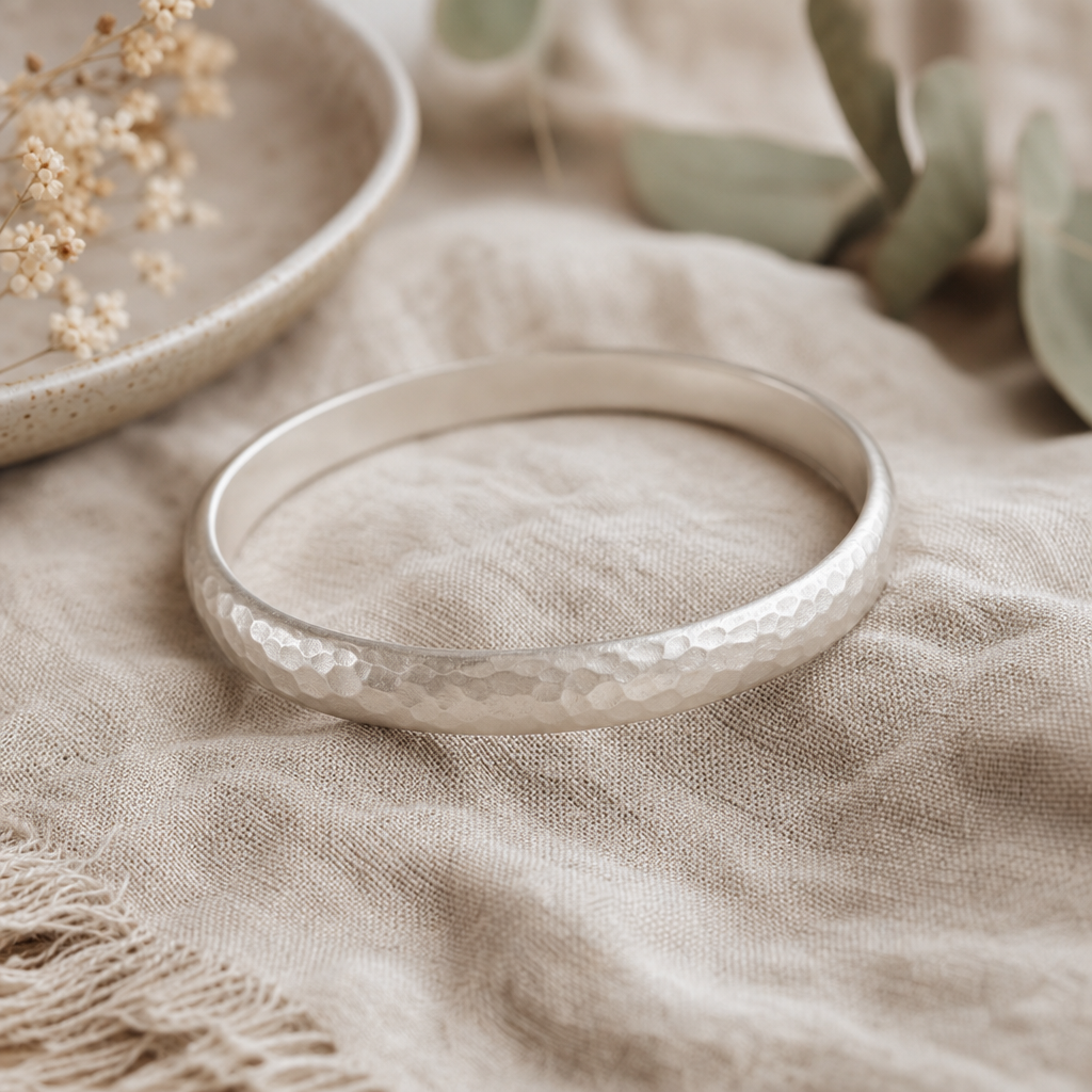 Matte silver bangle with a soft hammered texture resting on linen fabric