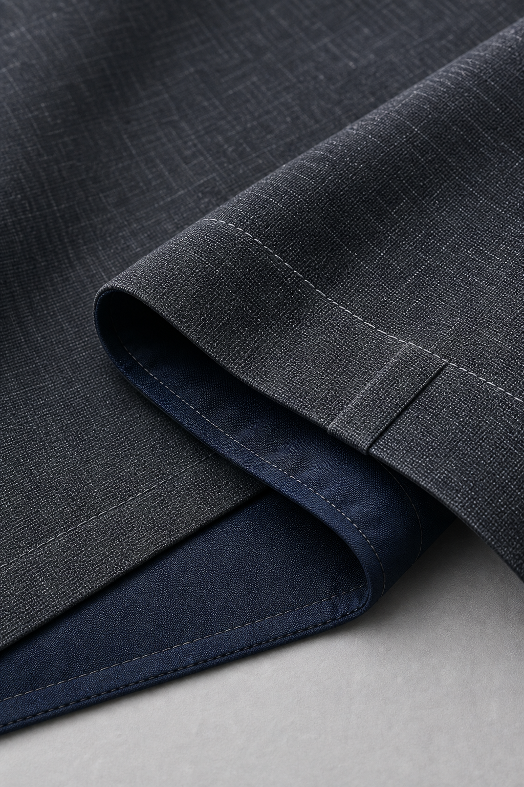 Close-up detail of premium curtain fabric with precise stitching, clean hem finish, and aligned weave pattern on a neutral work surface