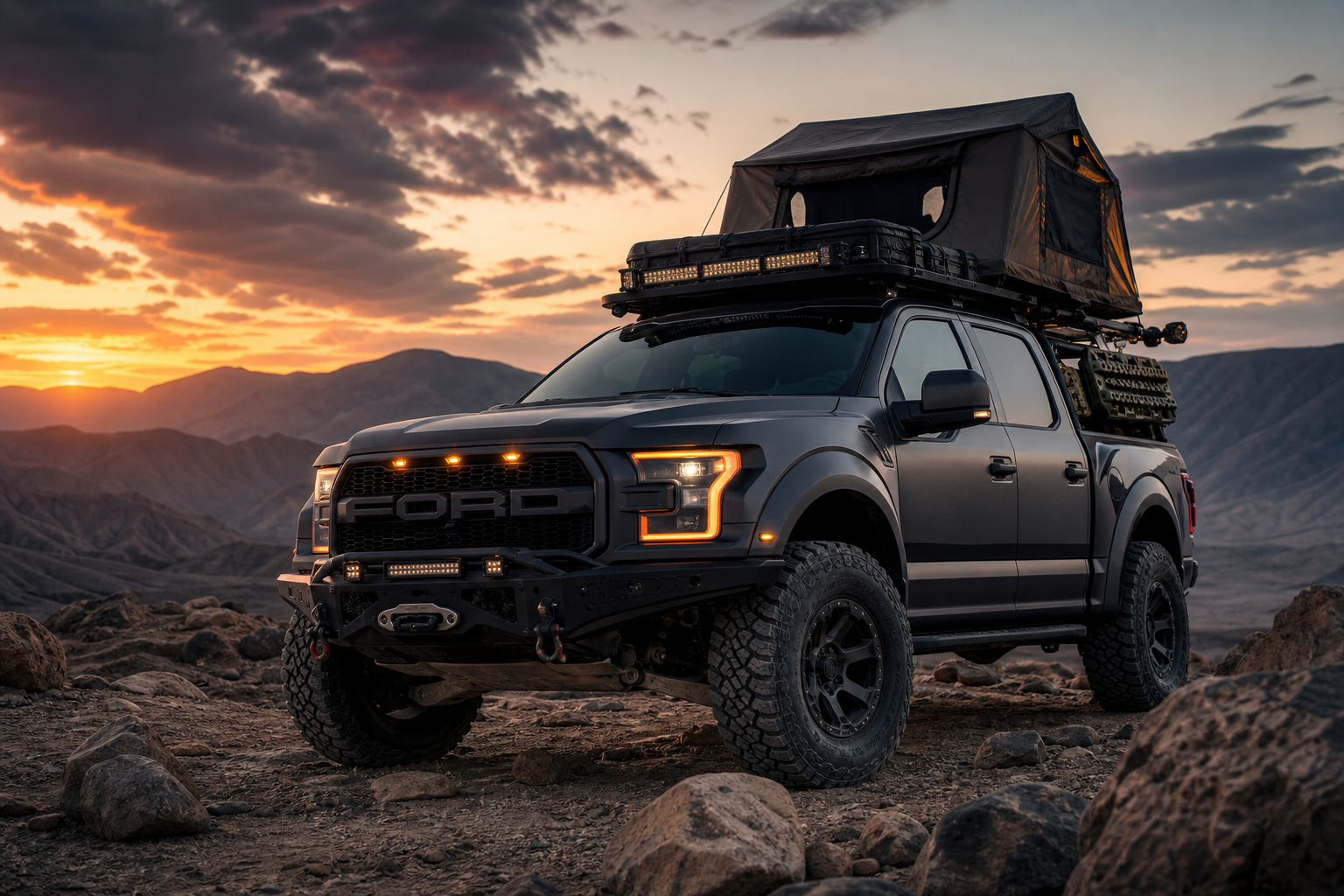 Matte charcoal Ford Raptor overland build with rooftop tent and amber grille lights parked on a rocky ridge at dusk