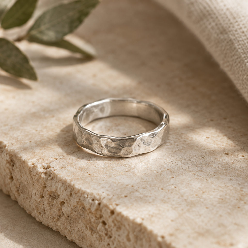 Hand-forged sterling silver ring with a softly irregular hammered band on a warm neutral stone surface