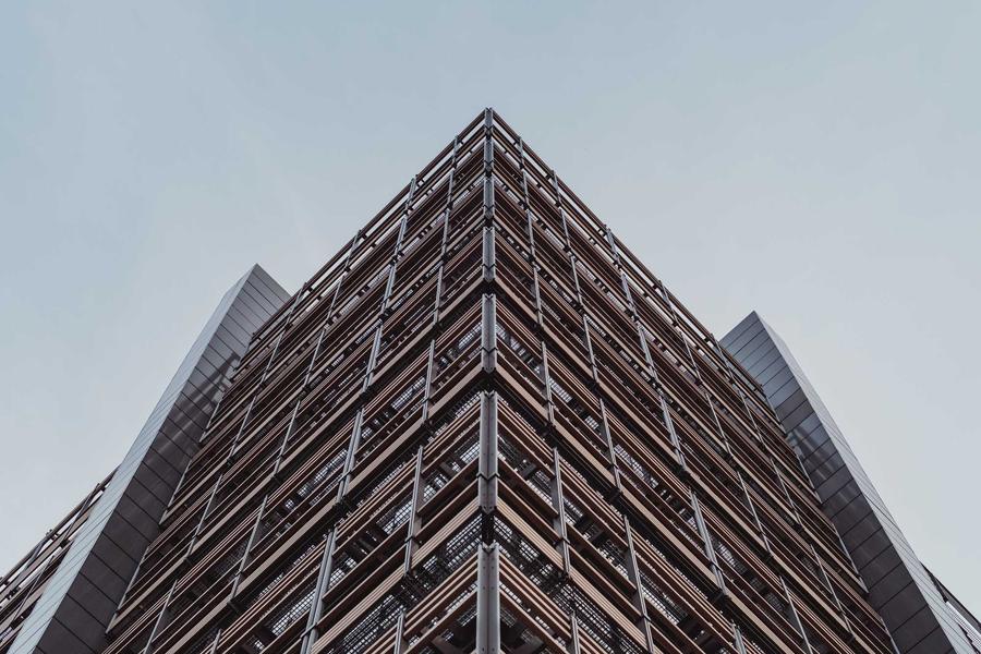 Angular modern building facade seen from below against a pale sky