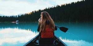 Woman in a red jacket paddling a canoe on a calm lake