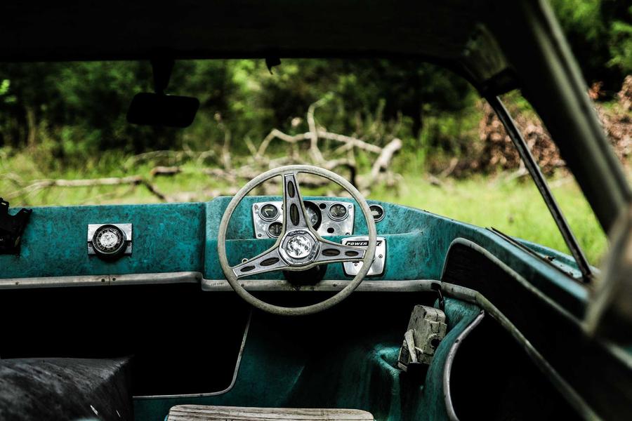 Dark close-up of the dashboard and chrome steering wheel of a vintage car