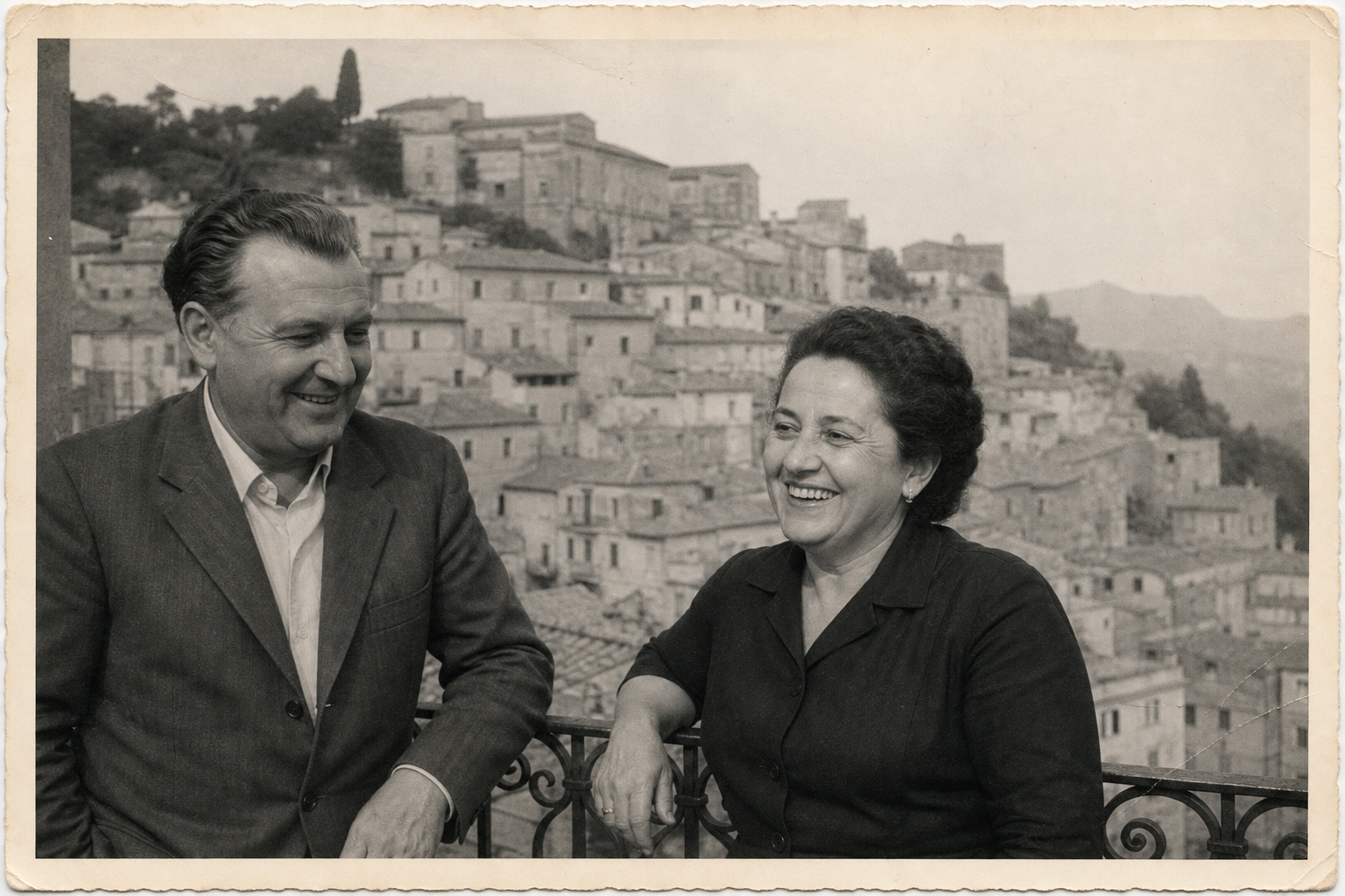 Black-and-white candid photo of two relatives smiling beside a balcony railing during a summer visit