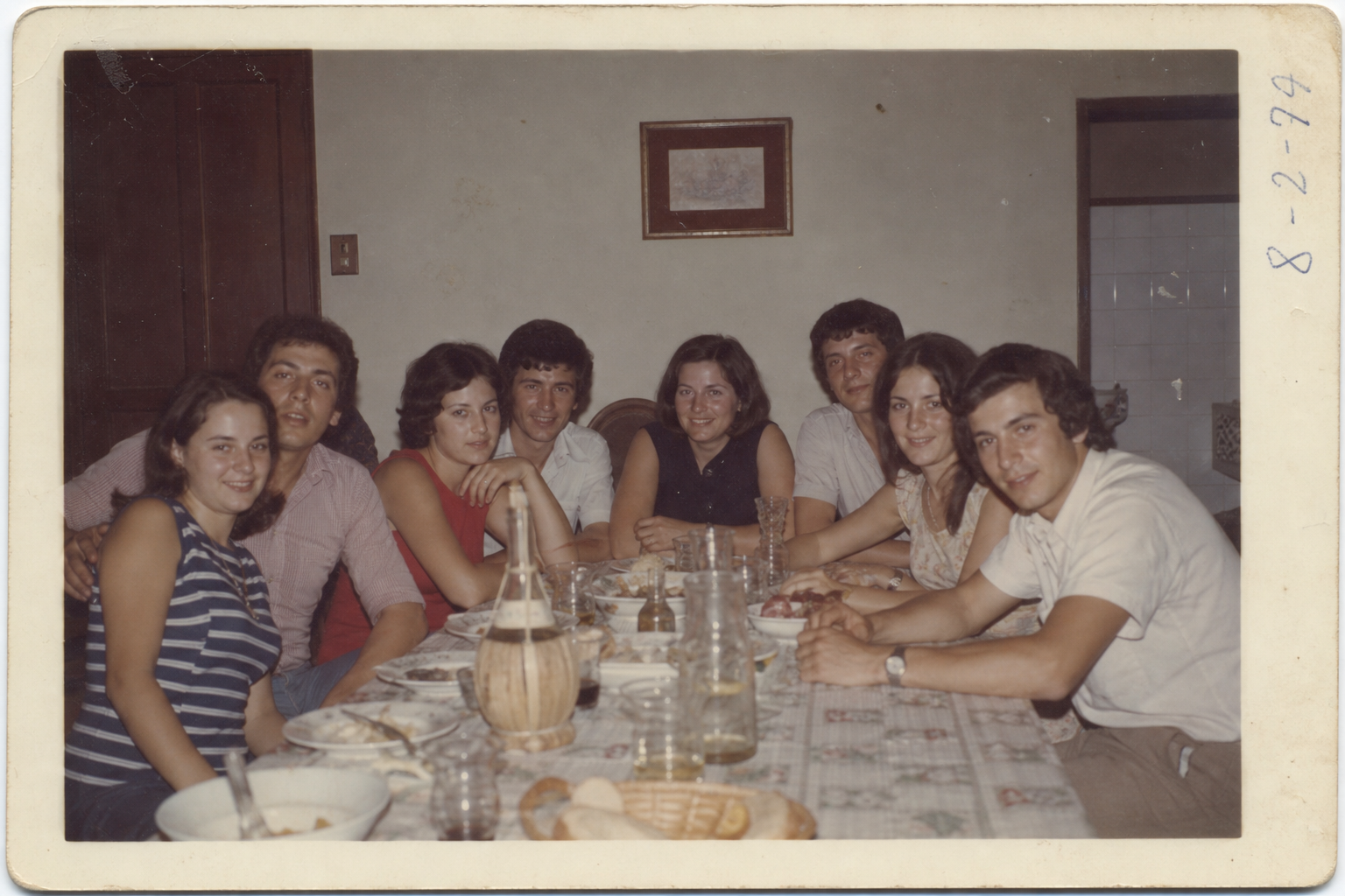 Faded color photograph of cousins seated at a long dining table with handwritten date notes on the edge