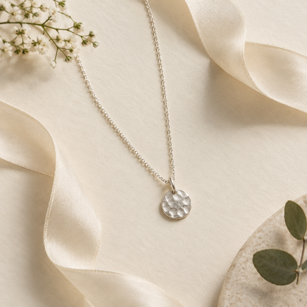 Delicate silver pendant necklace arranged in a soft ivory flat lay with silk ribbon