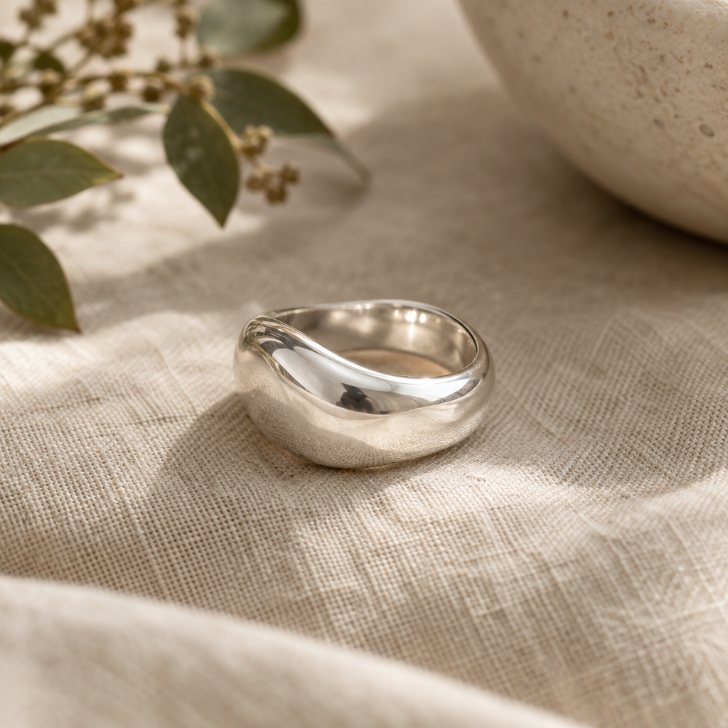 Close-up of a sculptural polished silver statement ring on a warm linen surface