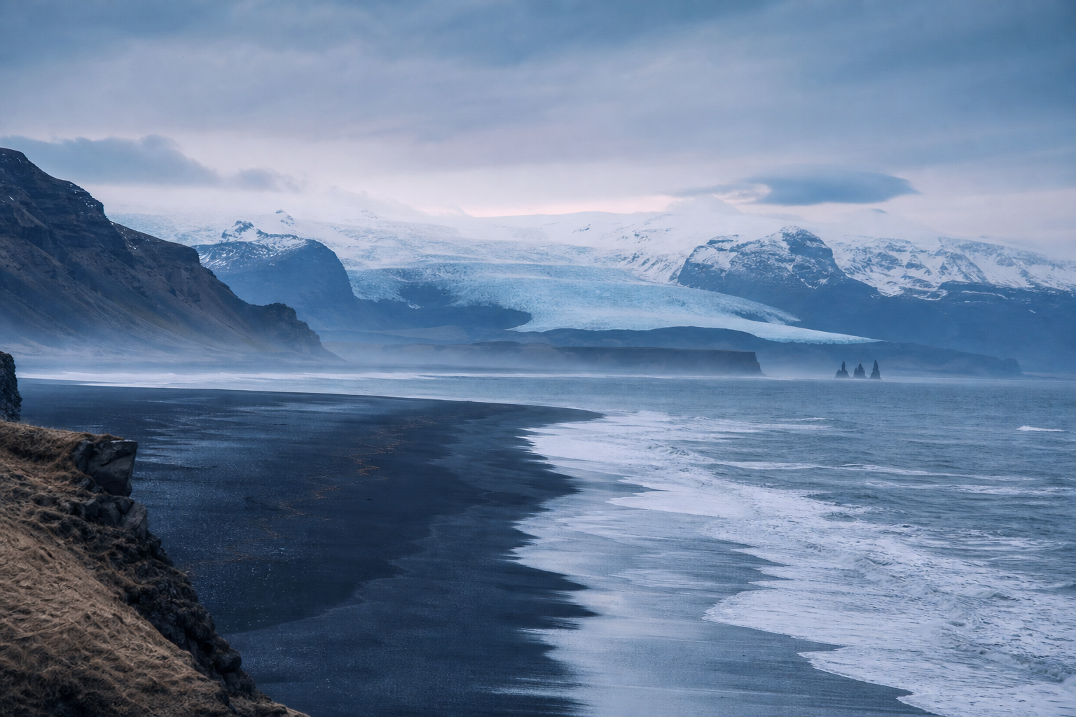 Misty black sand coastline of Iceland's Ring Road with distant glacier light