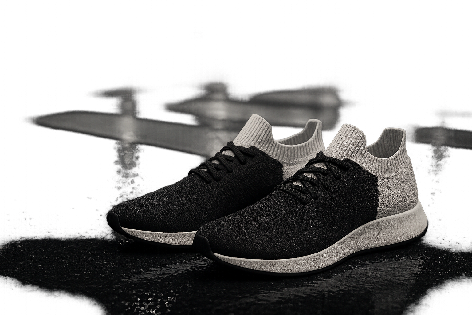 Transit Knit black and bone sneaker pair styled in a night street-crosswalk campaign scene with wet pavement reflections