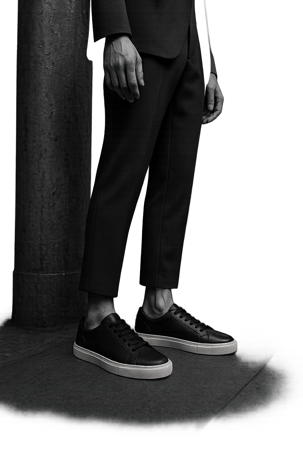 Streetwear portrait on a concrete subway platform highlighting monochrome low-top sneakers and tailored trousers