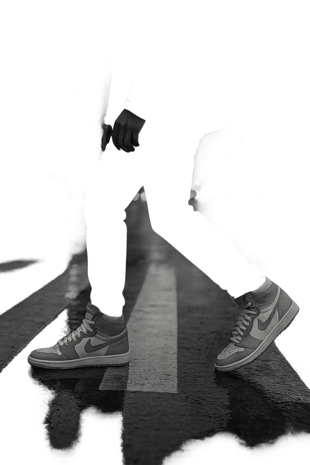 Monochrome urban lifestyle scene of a sneaker enthusiast striding across a wet crosswalk at dusk, with textured asphalt reflections and motion blur from city lights