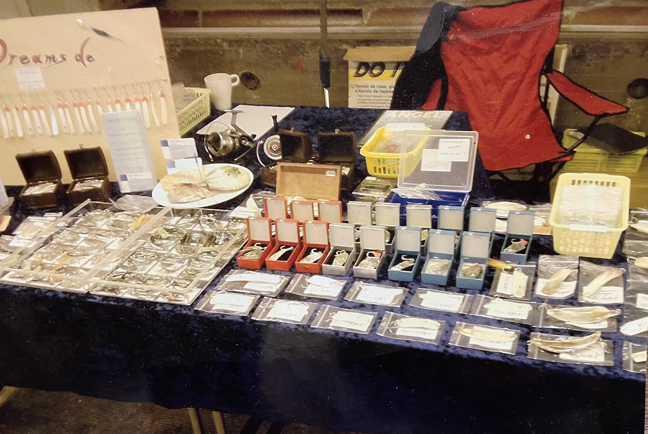 Auslage mit verpackten Angel- und Tackle-Artikeln auf einem Tisch, inklusive Ködern, Boxen und Zubehör