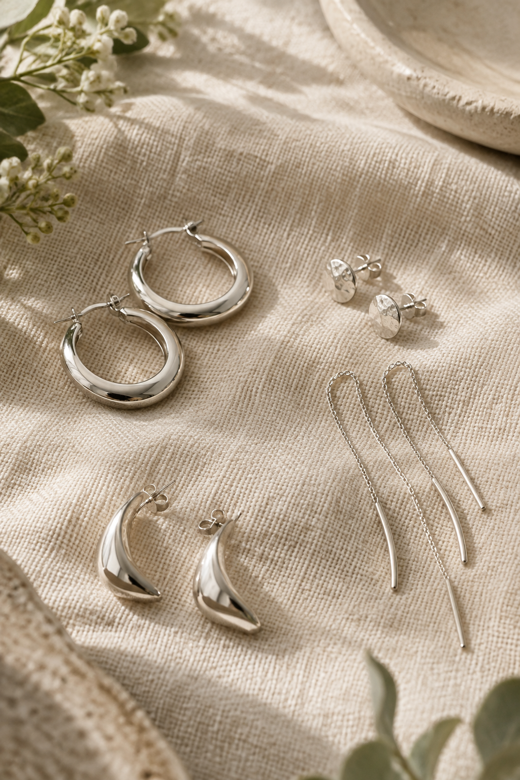 Small sculptural sterling silver hoop earrings on soft woven fabric