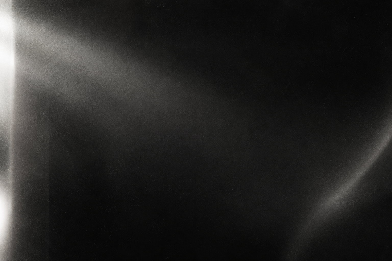 Abstract monochrome film texture with subtle grain, light leak haze, and cinematic shadow gradients