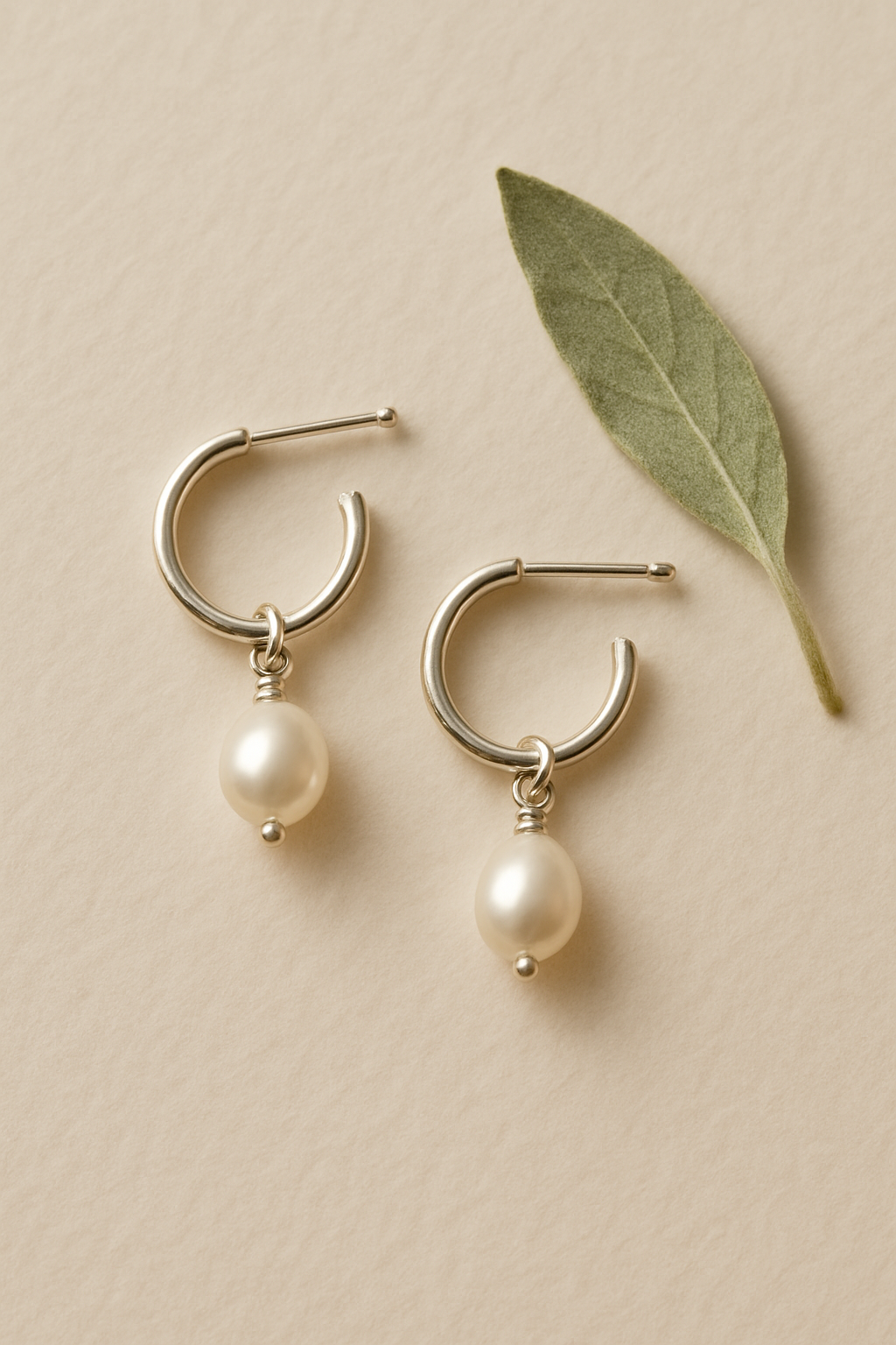 Pair of small silver hoop earrings with tiny freshwater pearl drops on a cream paper background