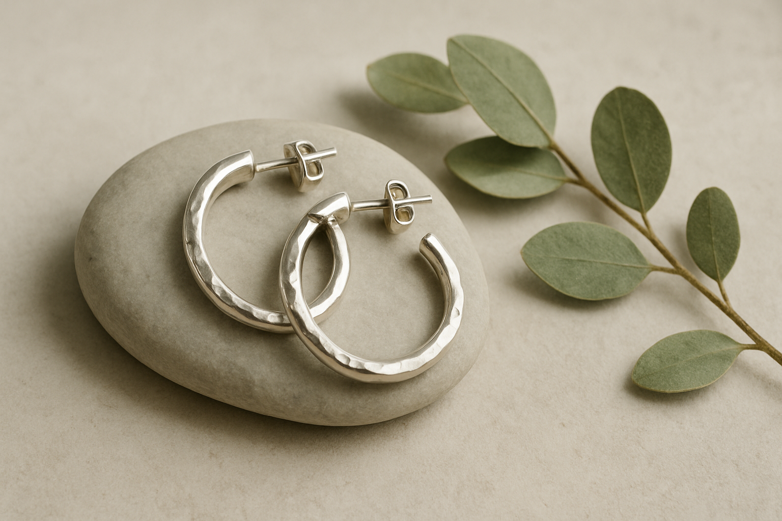 Pair of hammered silver hoop earrings laid on a smooth pale river stone