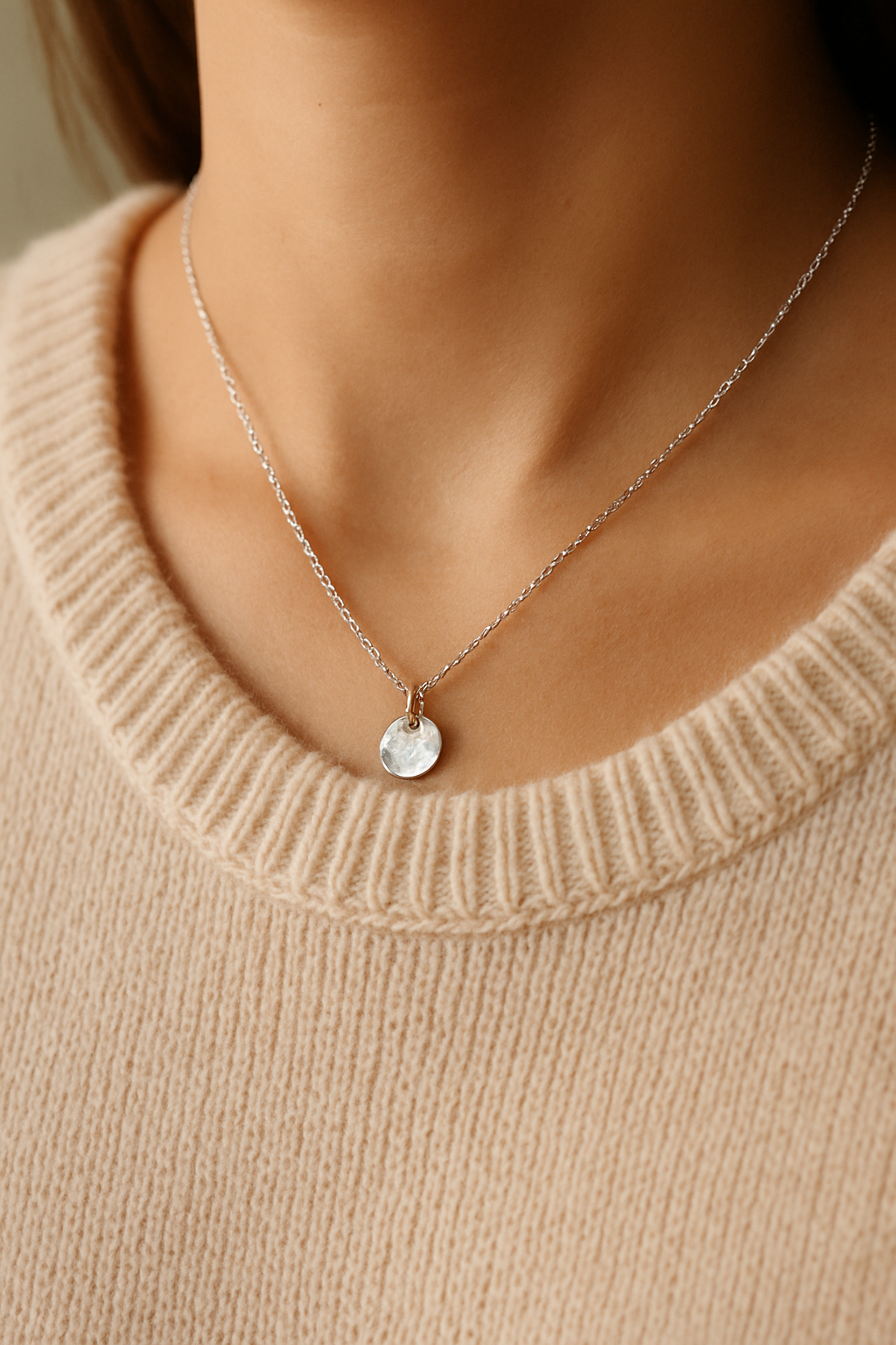 Delicate silver chain necklace with a small hammered disc pendant worn at the collarbone