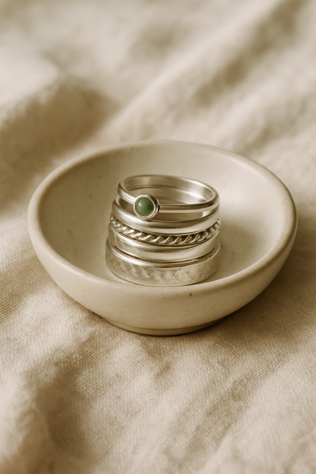 Stack of handmade sterling silver rings resting in a small ceramic dish on natural linen