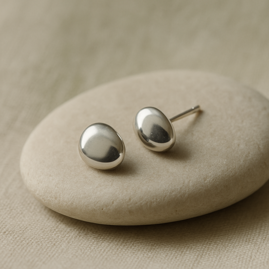 Small organic pebble-shaped silver stud earrings on pale stone