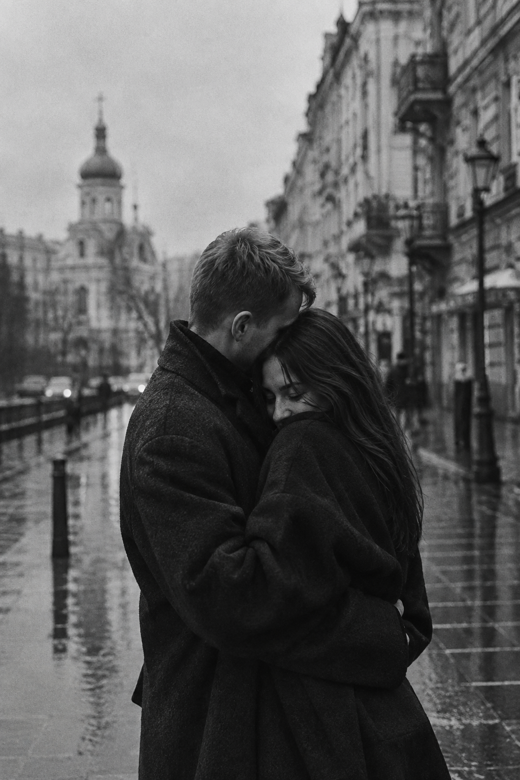 Black-and-white film-style photograph of a couple in dark coats embracing on a rain-washed city street