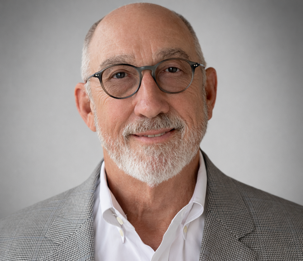 Professional headshot of an experienced male sales leader wearing glasses, a white shirt, and a gray blazer against a neutral background